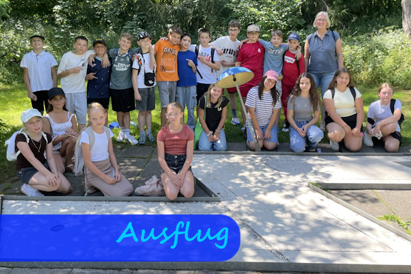 Hinter der Bahn einer Minigolfanlage stehen Kinder mit ihrer Lehrerin zu einem Gruppenfoto beisammen.