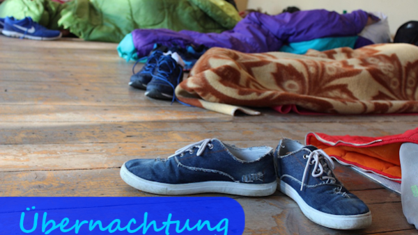 Schlafsäcke liegen in einem Raum auf dem Boden, im Vordergrund steht ein Paar Schuhe.