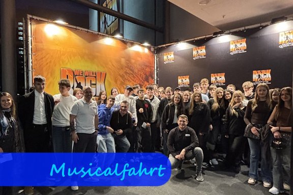 Vor einem großen Plakat des Musicals "We will rock you" stehen Jugendliche zu einem Gruppenbild zusammen.