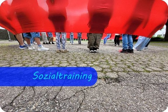 Ein rotes, breites elastisches Band zieht sich am oberen Bildrand entlang. Darin lehnen Kinder, deren Silouetten durch den Stoff scheinen. Unterhalb des Bandes schauen die Beine der stehenden Kinder heraus.