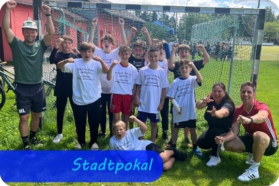 Vor einem Kleinfeldfußballtor stehen und knien jubelnd die Jungen mit drei Erwachsenen und zeigen Jubelposen.