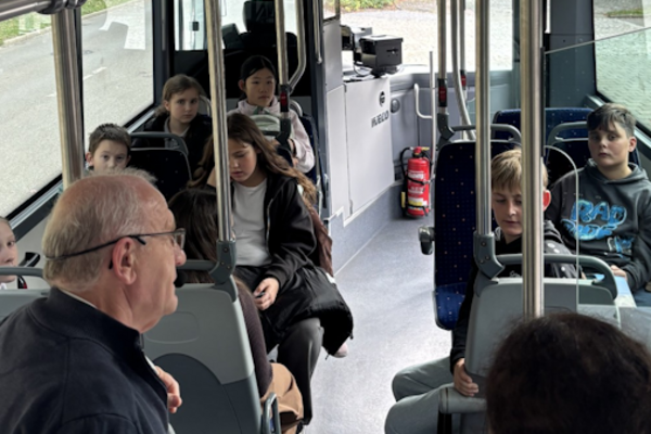 Ein Bus mit Kindern und einer Person im Vordergrund, die den Kindern etwas erklärt.