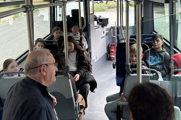 Ein Bus mit Kindern und einer Person im Vordergrund, die den Kindern etwas erklärt.