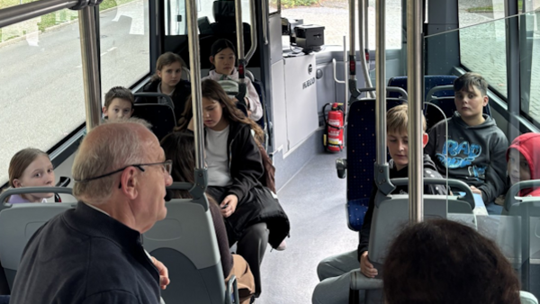 Ein Bus mit Kindern und einer Person im Vordergrund, die den Kindern etwas erklärt.