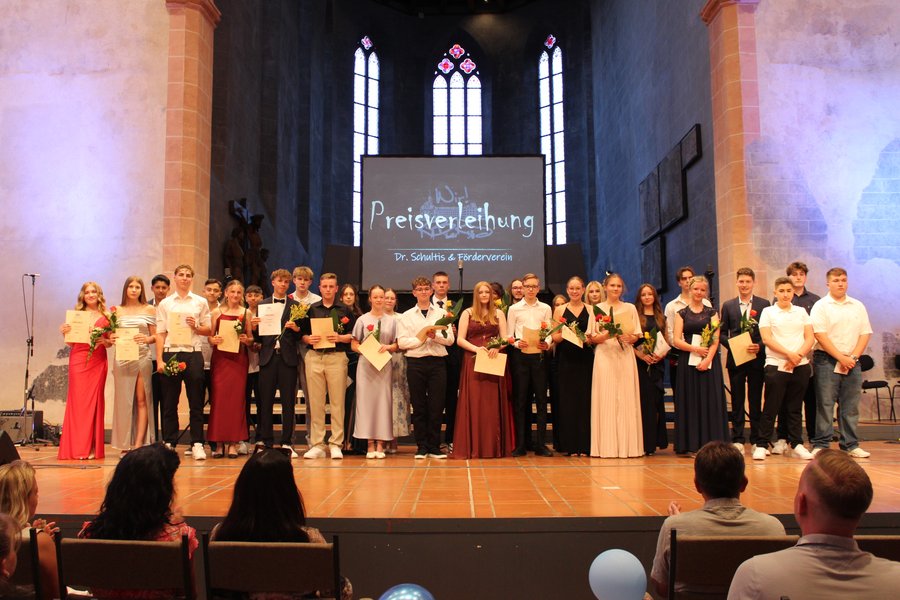 Auf der Bühne stehen weibliche und männliche Jugendliche mit Urkunden und Blumen in der Hand zum Foto zusammen.