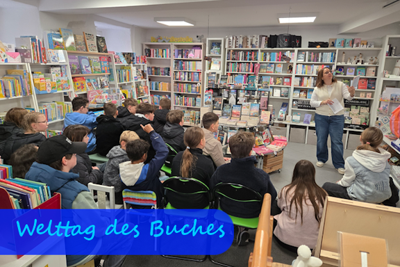 In einer Buchhandlung mit Büchern in den Regalen an den Wänden sitzen Kinder mit dem Rücken zur Kamera auf kleinen Stühlen. Sie hören einer Frau zu, die ein Buch in der Hand hält.