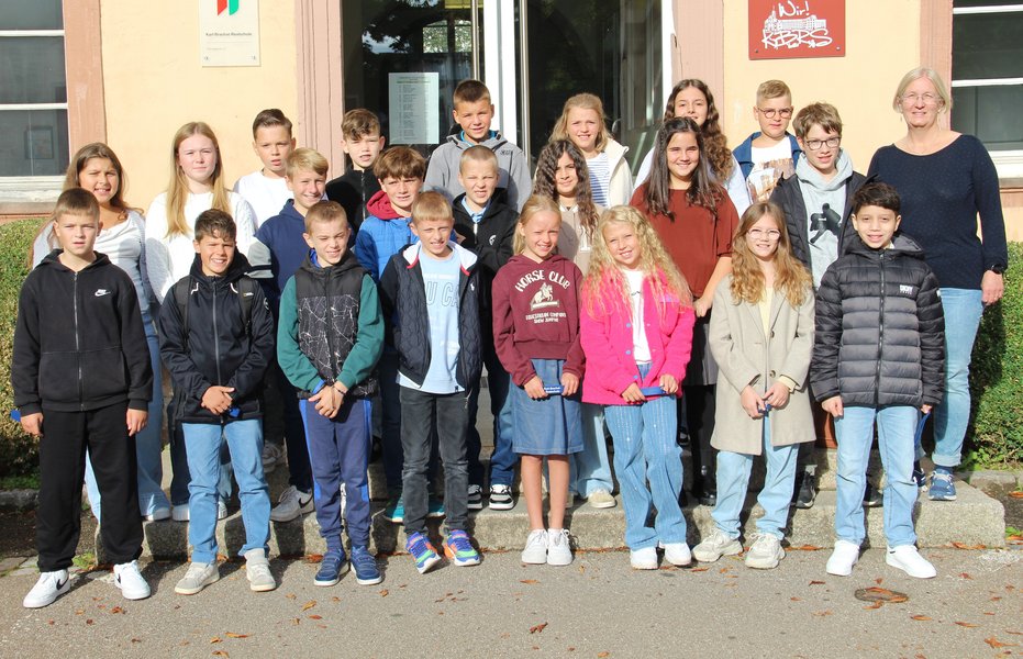 Vor dem Eingang der Schule hat sich eine fünfte Klasse mit den Klassenlehrkräften zum Gruppenfoto aufgestellt.