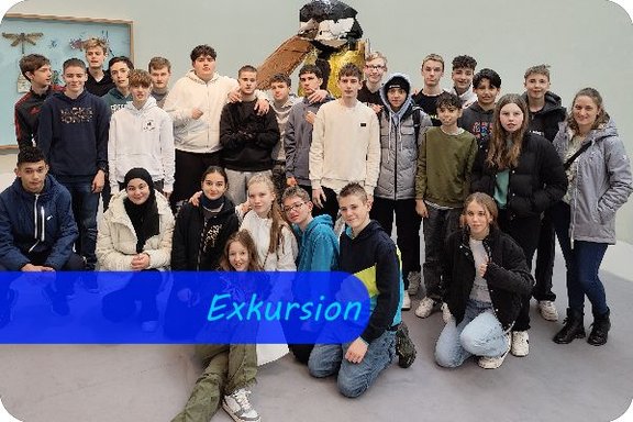 Eine Schulklasse hat sich für ein Gruppenfoto vor einer Vogelskulptur aus Recyclingmaterialien aufgestellt.