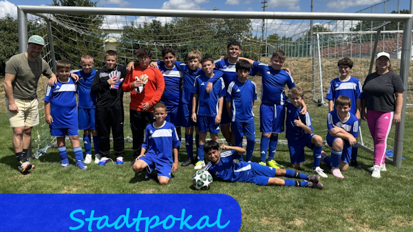 Vor einem Fußballtor haben sich Jungen in blauen Trikots zu einem Mannschaftsfoto aufgestellt, davor kniet und liegt jeweils ein Jungen. Links und rechts stehen eine männliche und eine weibliche Lehrkraft.