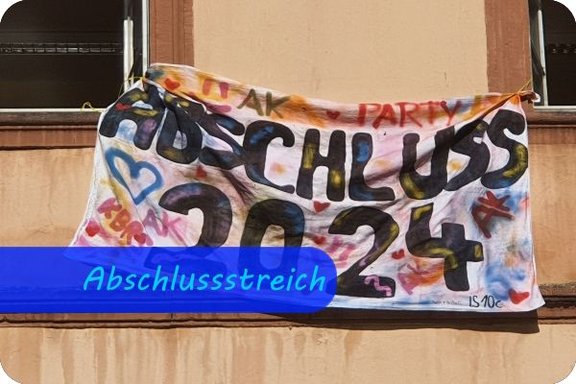 Abschlussstreich 2024 Zwischen zwei offenen Fenstern hängt über einer beigen Hauswand ein bunt bemaltes Laken. Darauf steht: "Abschluss 2024"