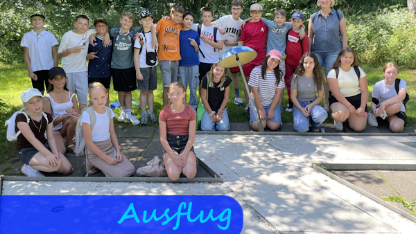 Hinter der Bahn einer Minigolfanlage stehen Kinder mit ihrer Lehrerin zu einem Gruppenfoto beisammen.