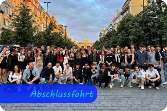 Gruppenbild einer Schülergruppe. Im Hintergrund verläuft eine Straße gesäumt von Häusern.