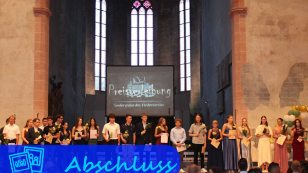 Auf der Bühne vor einem kirchenähnlichen Flügel stehen Jugendliche in Abendgarderobe mit Urkunden/Zeugnissen in der Hand zum Gruppenfoto bereit.