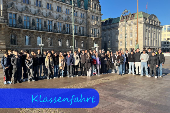 Unsere Klassen 10a und 10b mit den Begleitlehrkräften in Hamburg Auf einem Platz vor zwei gr0ßen Gebäuden stehen die Schülerinnen und Schüler als Gruppe, um fotografiert zu werden. Die Lehrkräfte befinden sich etwa in der Mitte.