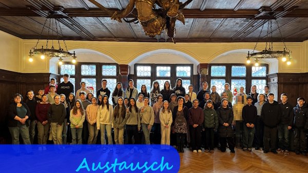 In einem mittelalterlich wirkendenden, holzvertäfelten Raum stehen Schülerinnen und Schüler vor großen Fenstern für ein Gruppenfoto.