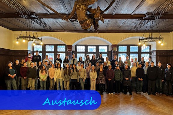 In einem mittelalterlich wirkendenden, holzvertäfelten Raum stehen Schülerinnen und Schüler vor großen Fenstern für ein Gruppenfoto.