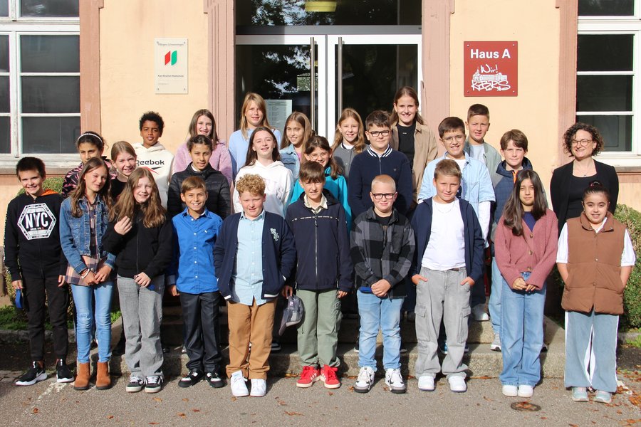 Vor dem Eingang der Schule hat sich eine fünfte Klasse mit den Klassenlehrkräften zum Gruppenfoto aufgestellt.