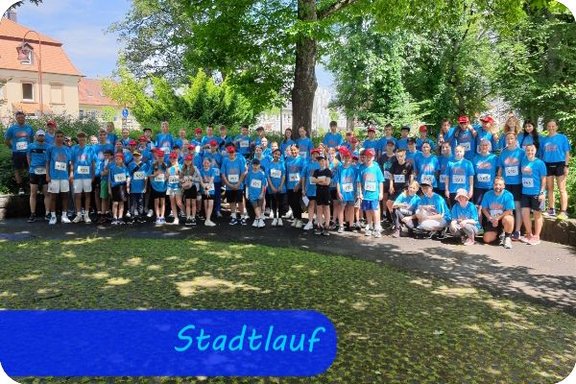 In drei Reihen stehen Kinder in blauen Sportshirts vor einer Grünanlage und sehen in die Kamera.