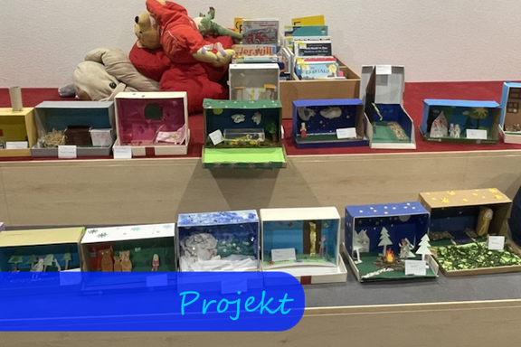 Auf Sitzstufen liegen Schuhkartons, die im Inneren Dioramen zu Märchen zeigen.