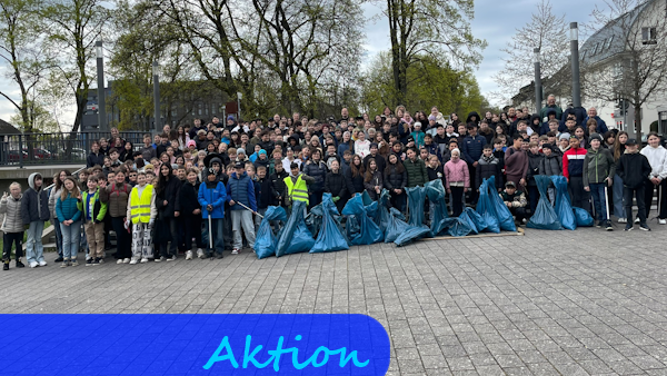 Eine große Gruppe Kinder steht für ein Gruppenfoto zusammen. Vor ihnen sind mehrere große, blaue Müllsäcke aufgereiht.