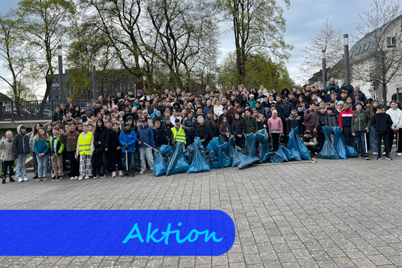 Eine große Gruppe Kinder steht für ein Gruppenfoto zusammen. Vor ihnen sind mehrere große, blaue Müllsäcke aufgereiht.
