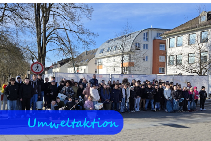 Vor einem Bauzaun stehen viele Schülerinnen und Schüler zum Gruppenfoto. Zum Teil haben sie Zangen und Eimer in den Händen.