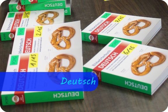Auf einem Holztisch liegen mehrere, gleiche, grün-weiße Bücher neben- und übereinander. Alle haben eine Brezel als Titelbild und am Rand steht die Aufschrift "Deutsch". Überschrift: Deutsch
