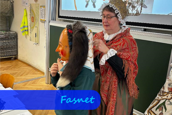 Eine Frau mit Haube und Tuch über den Schultern steht hinter einem Kind und hilft ihm eine Fasnachtsmaske aufzusetzen.